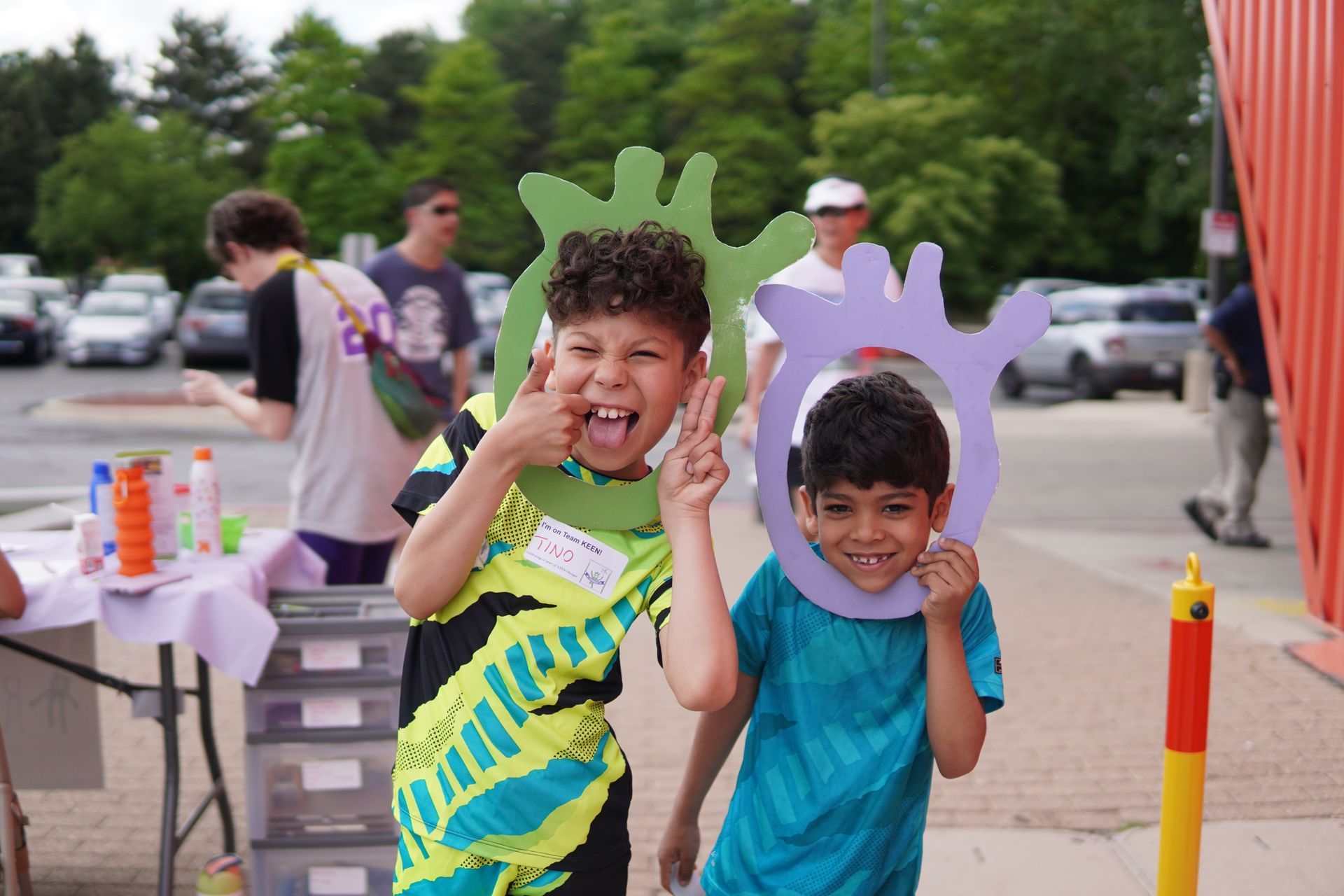 Two sibling attendees pose together. They are sticking their heads through foam boards of the Any K Ken logo.