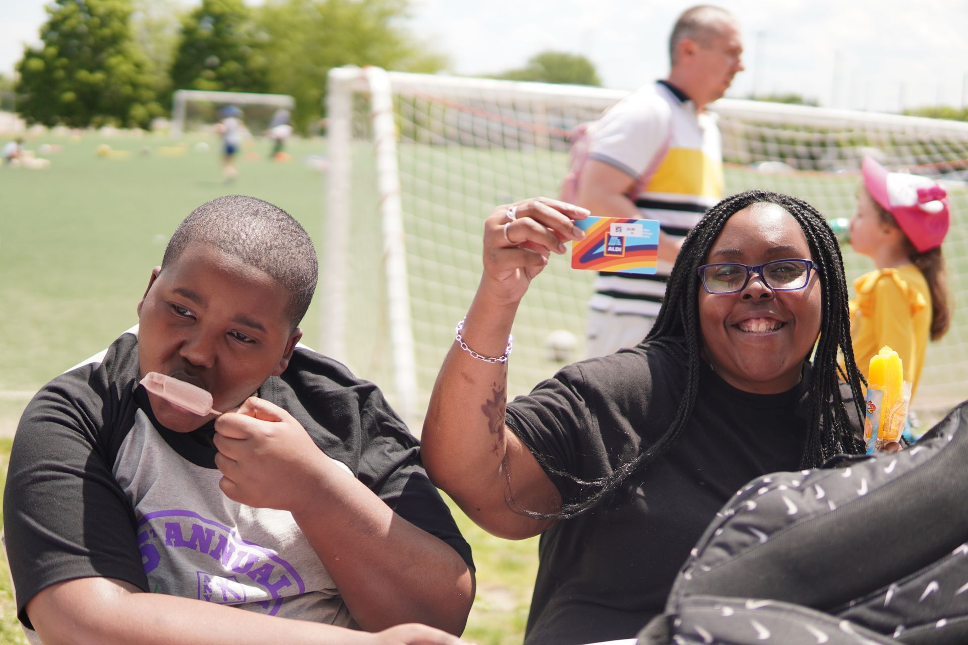 A mother and her son pose together. The mom holds up an Aldi giftcard she just won while her son eats a paleta.