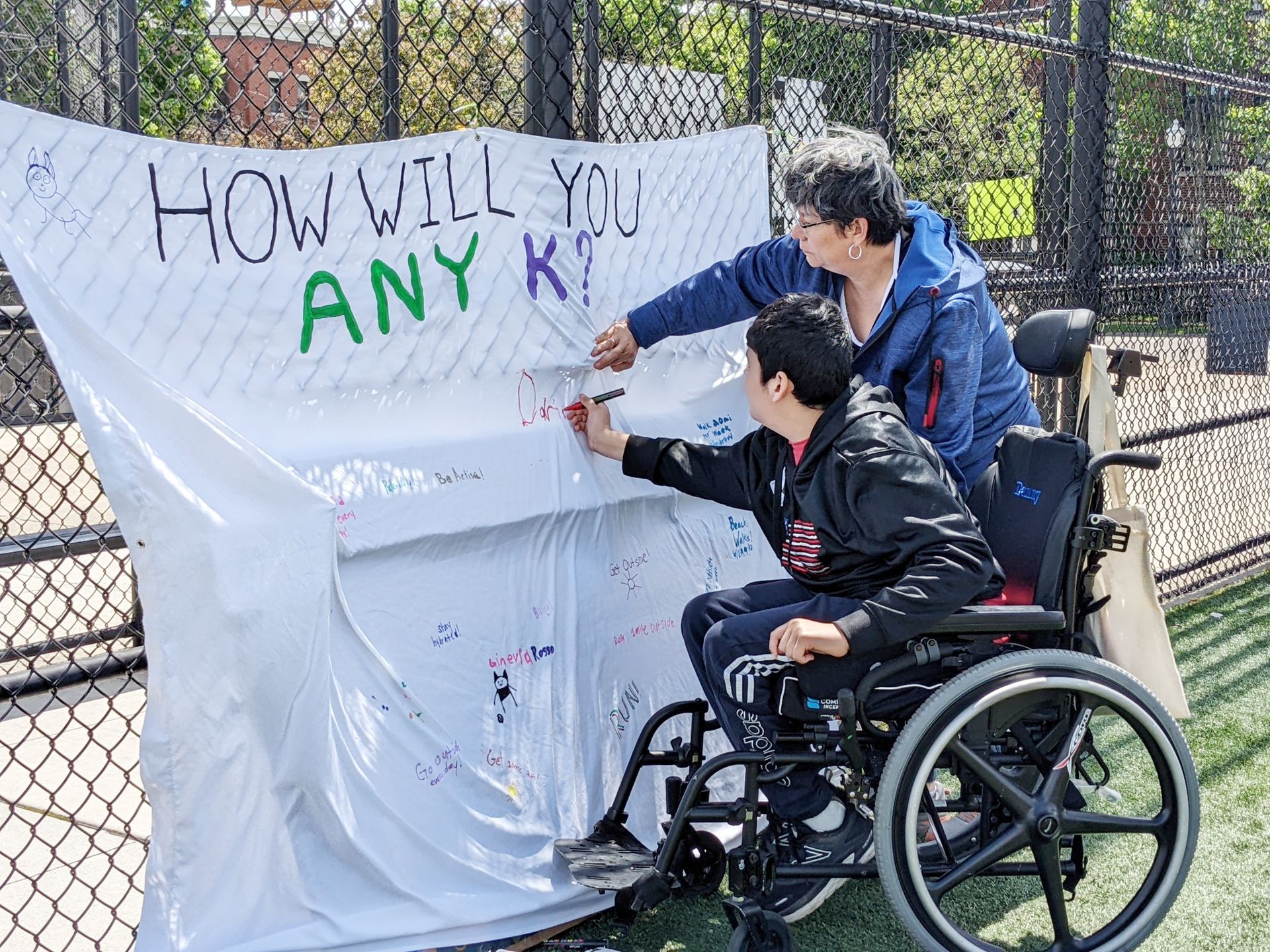 Athlete in wheelchair and Parent writing on ANY K Banner