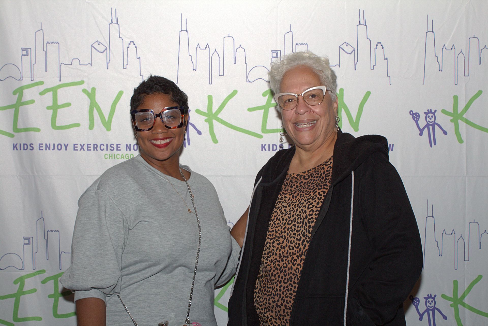 Two attendees pose in front of a logoed banner