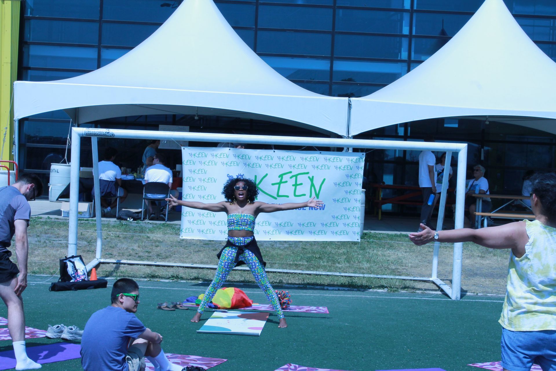 A yoga facilitator stands with arms and legs wide in front of a KEEN banner
