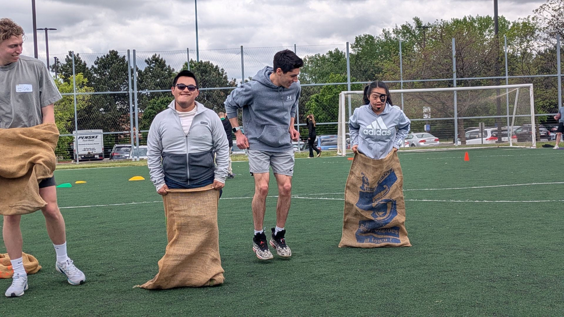 Athletes participate in a potato sack race supported by a volunteer
