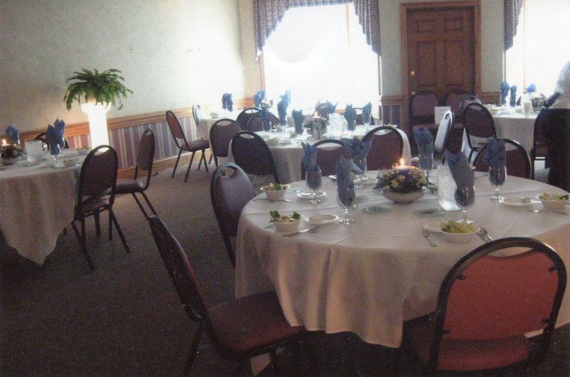 Dining room with round tables, white tablecloths, blue napkins, and flower centerpieces; brown chairs.