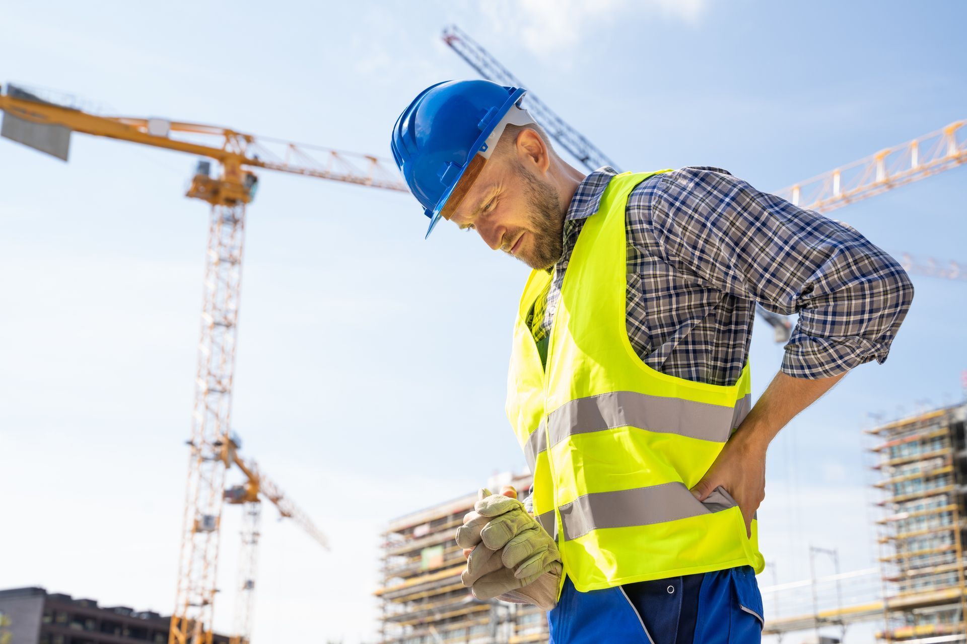 A construction worker is holding his back in pain at a construction site.