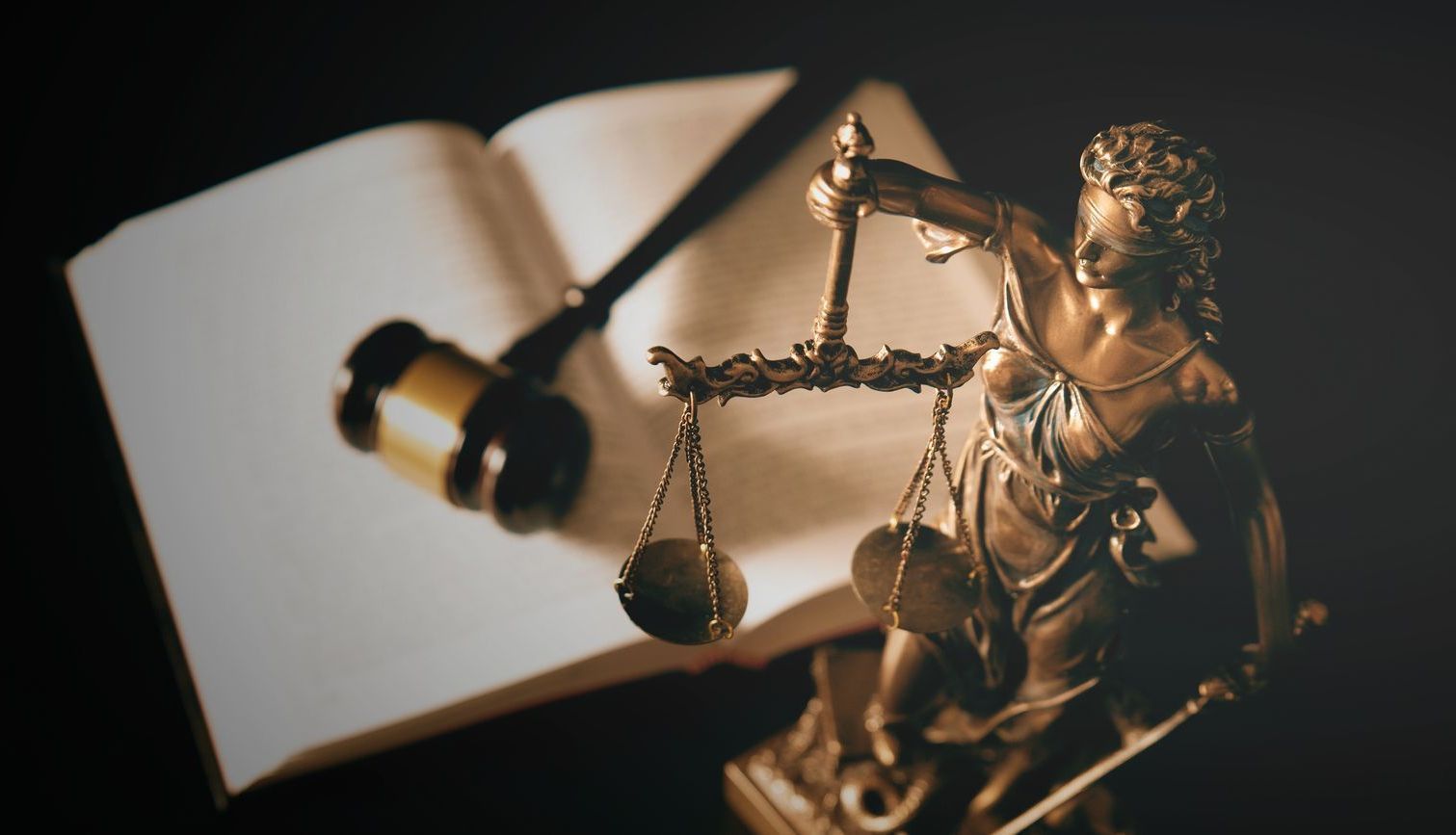 A statue of justice is sitting on top of an open book next to a gavel.