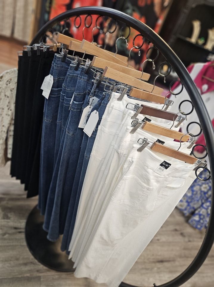 A clothing rack displays rows of jeans in black, blue, and white, in a boutique setting.
