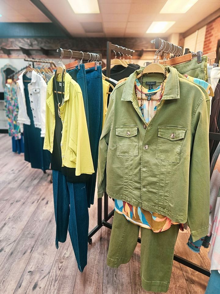 Clothing racks in a boutique showcase various outfits: jackets, blouses, and pants in colors like green, yellow, and blue.
