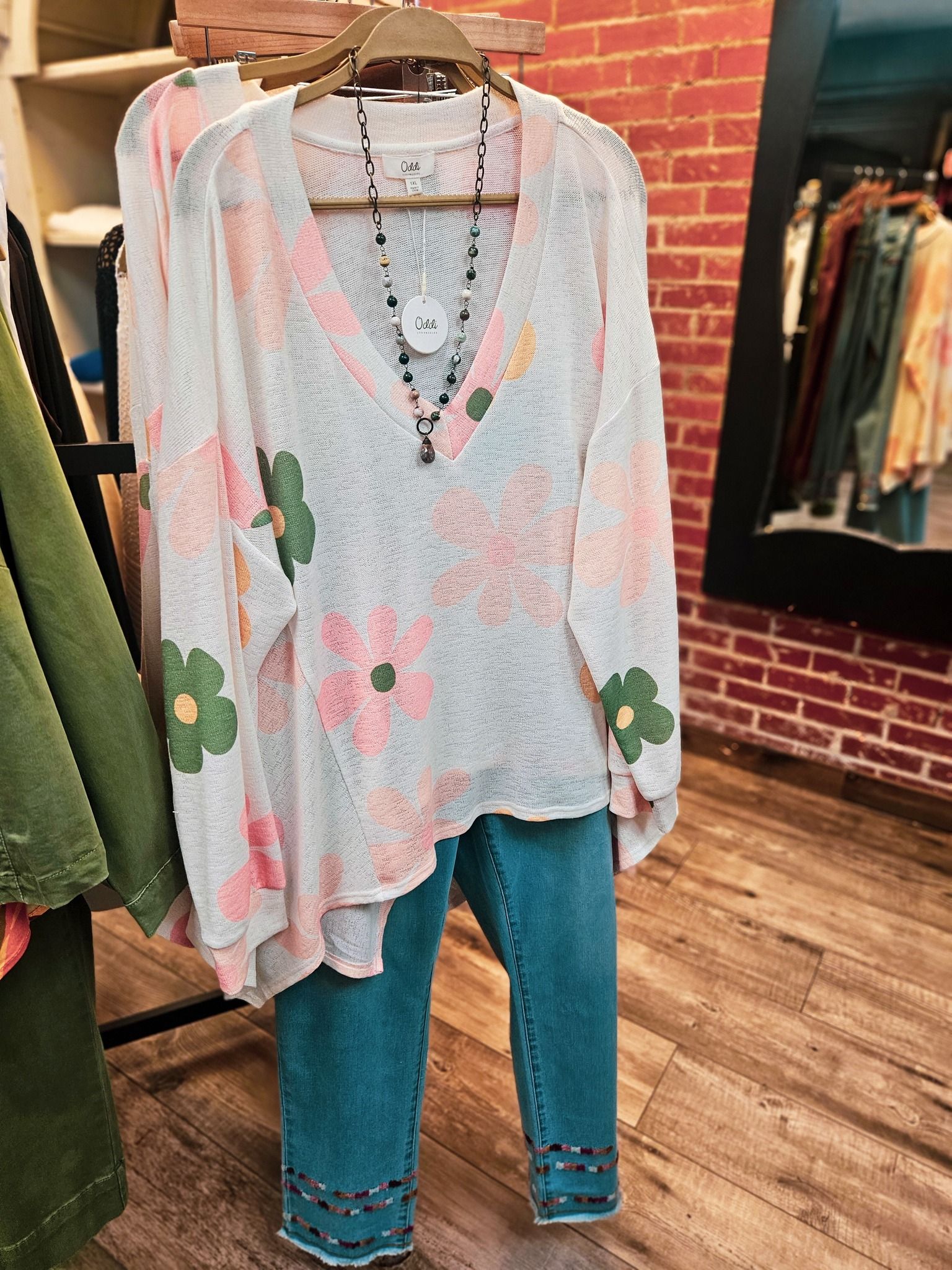 Floral, see-through top with jeans on a clothes rack in a boutique. A necklace hangs from the top.