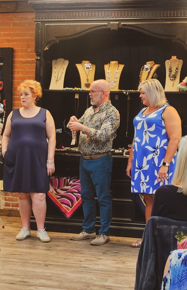 Three people interacting in a shop near a display of necklaces.