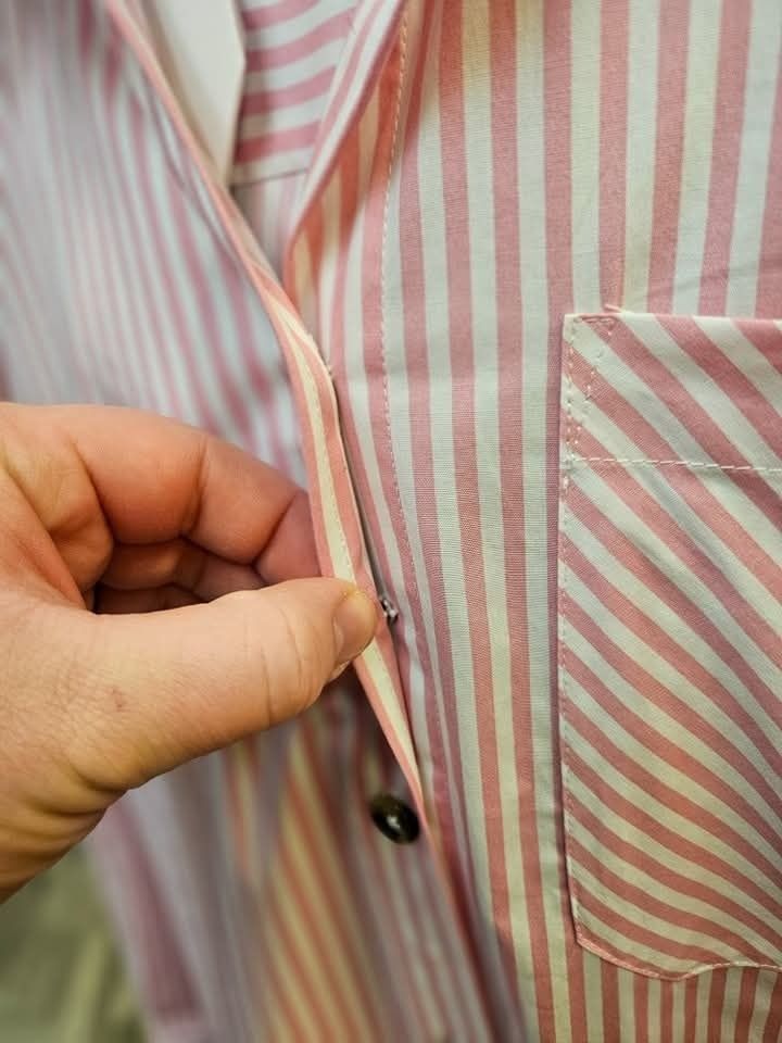 Person's hand fastening a button on a pink and white striped pajama top.