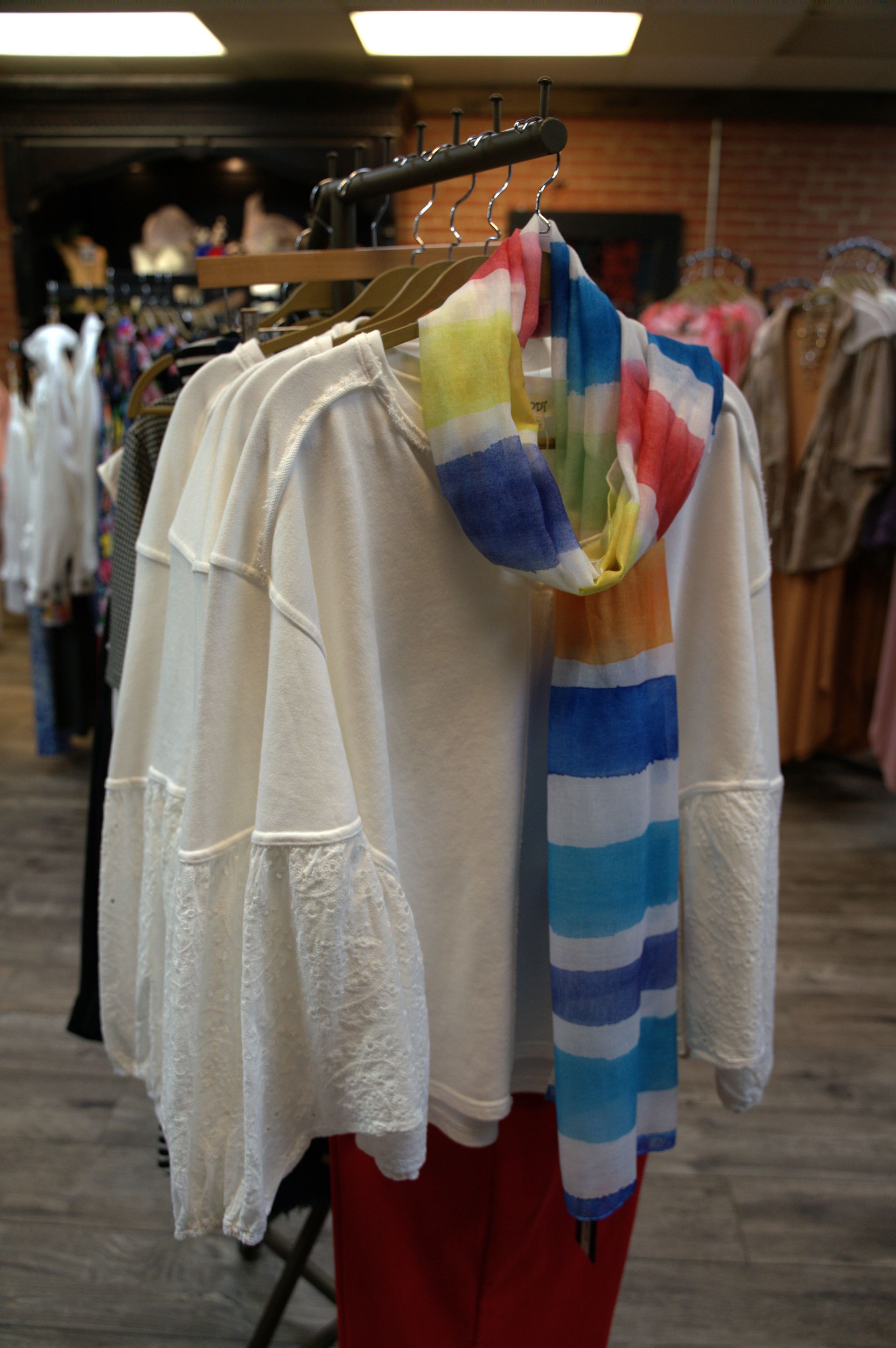 A white sweater with flared sleeves and a striped scarf hanging on a rack in a clothing store.