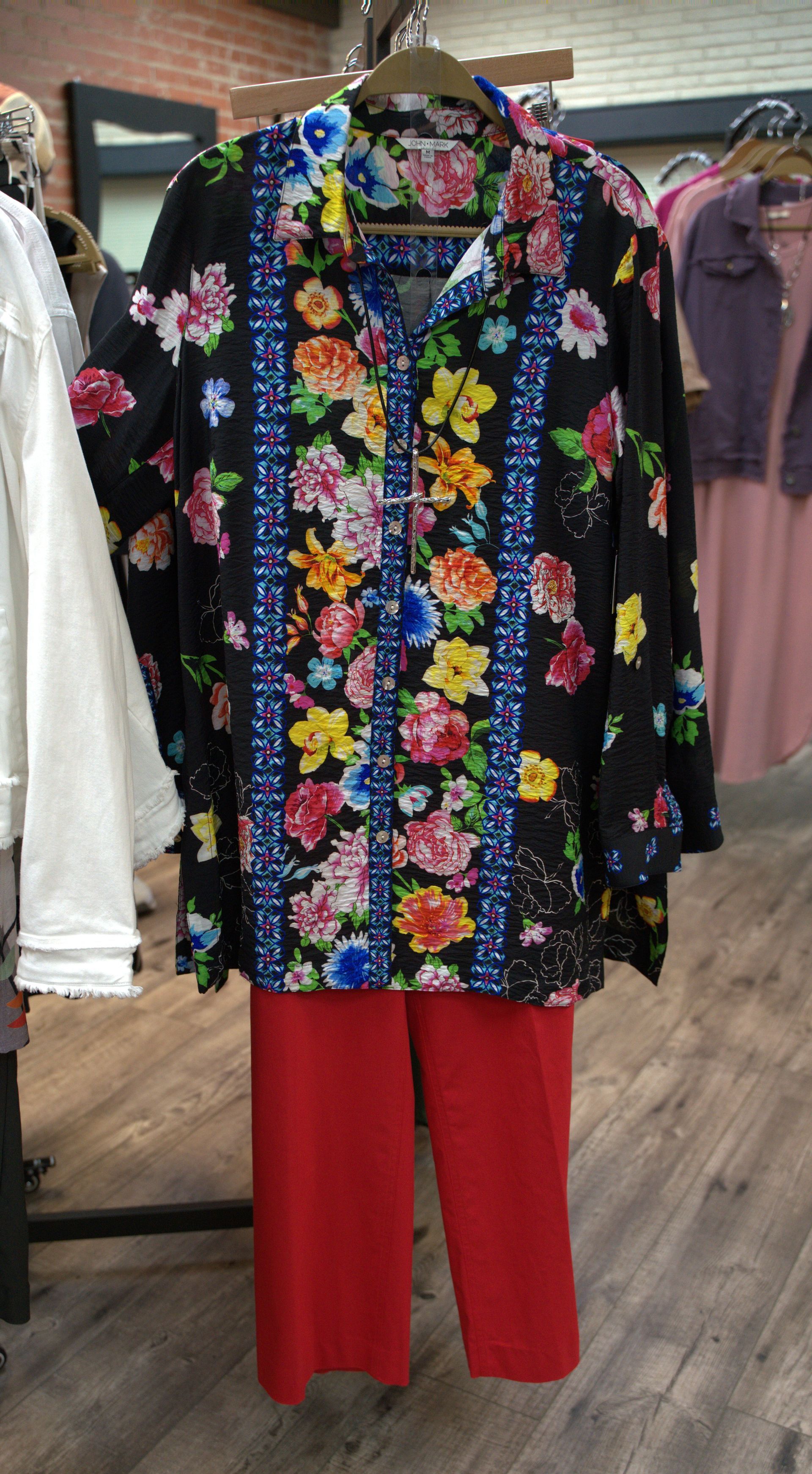 A black floral print shirt and red pants on a clothing rack in a store.