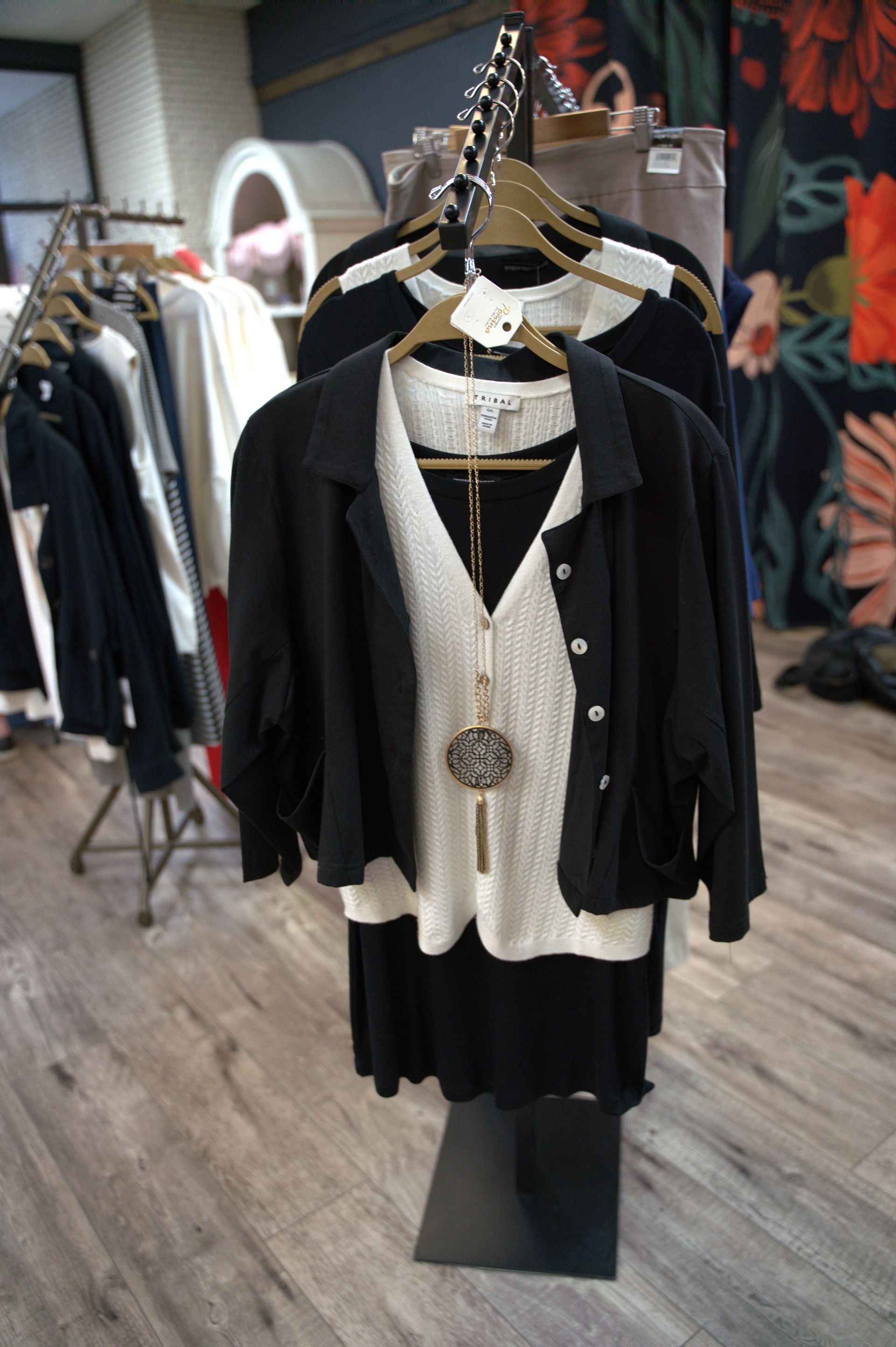 Clothing display in a boutique featuring black and white outfits on hangers, including a black jacket over a cream sweater.