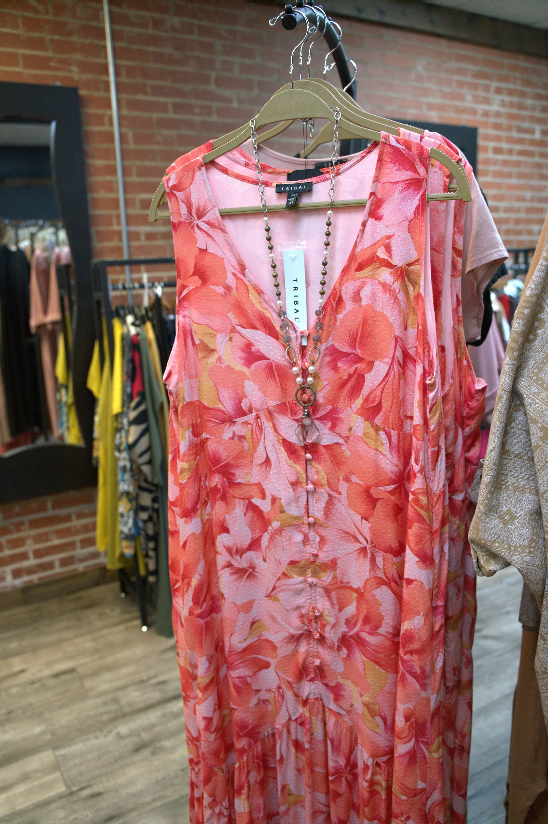 A long, flowing floral-print dress in shades of pink and orange hanging in a clothing store.
