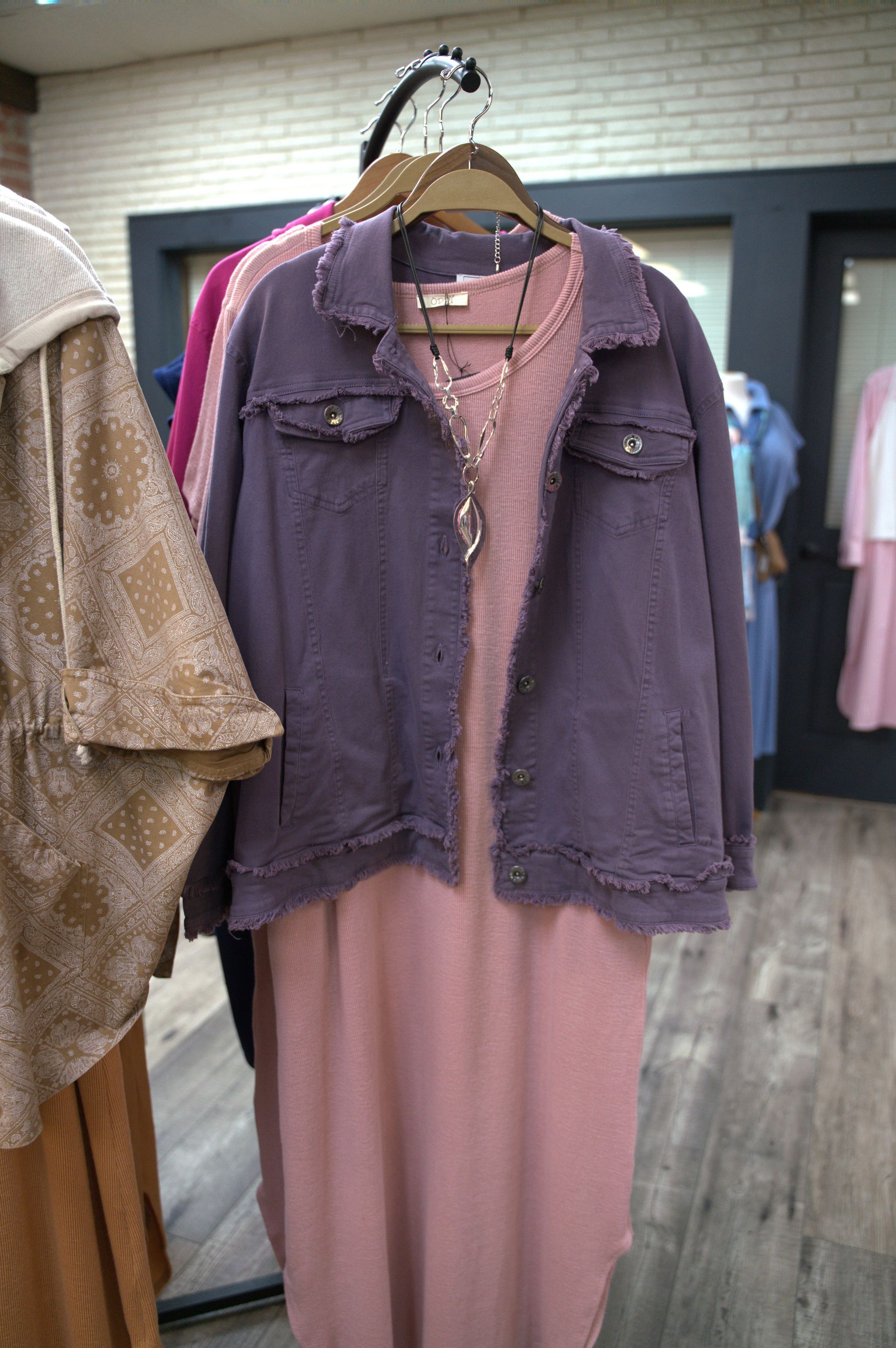 Purple denim jacket with frayed edges over a pink dress, displayed on a clothing rack.