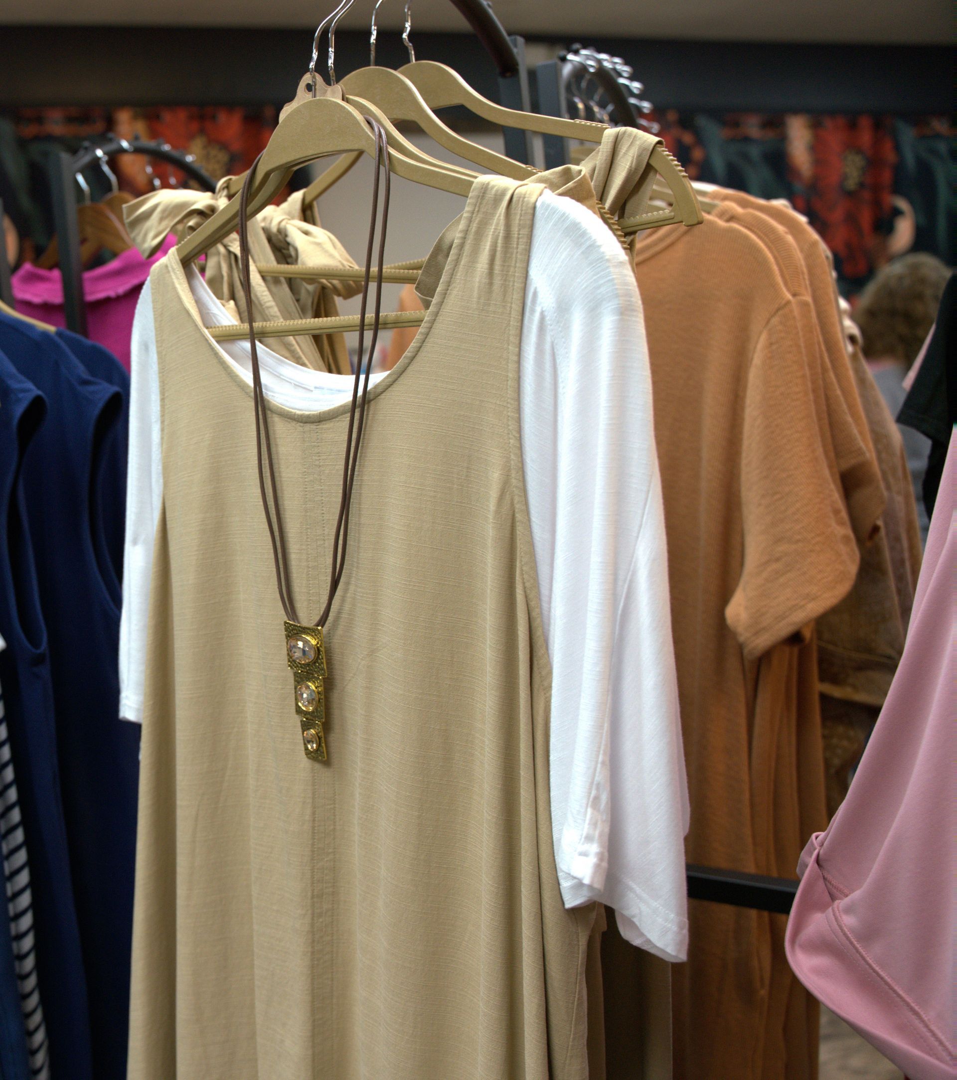 Clothing rack with several dresses; a gold-colored dress over a white long-sleeved shirt is in focus.