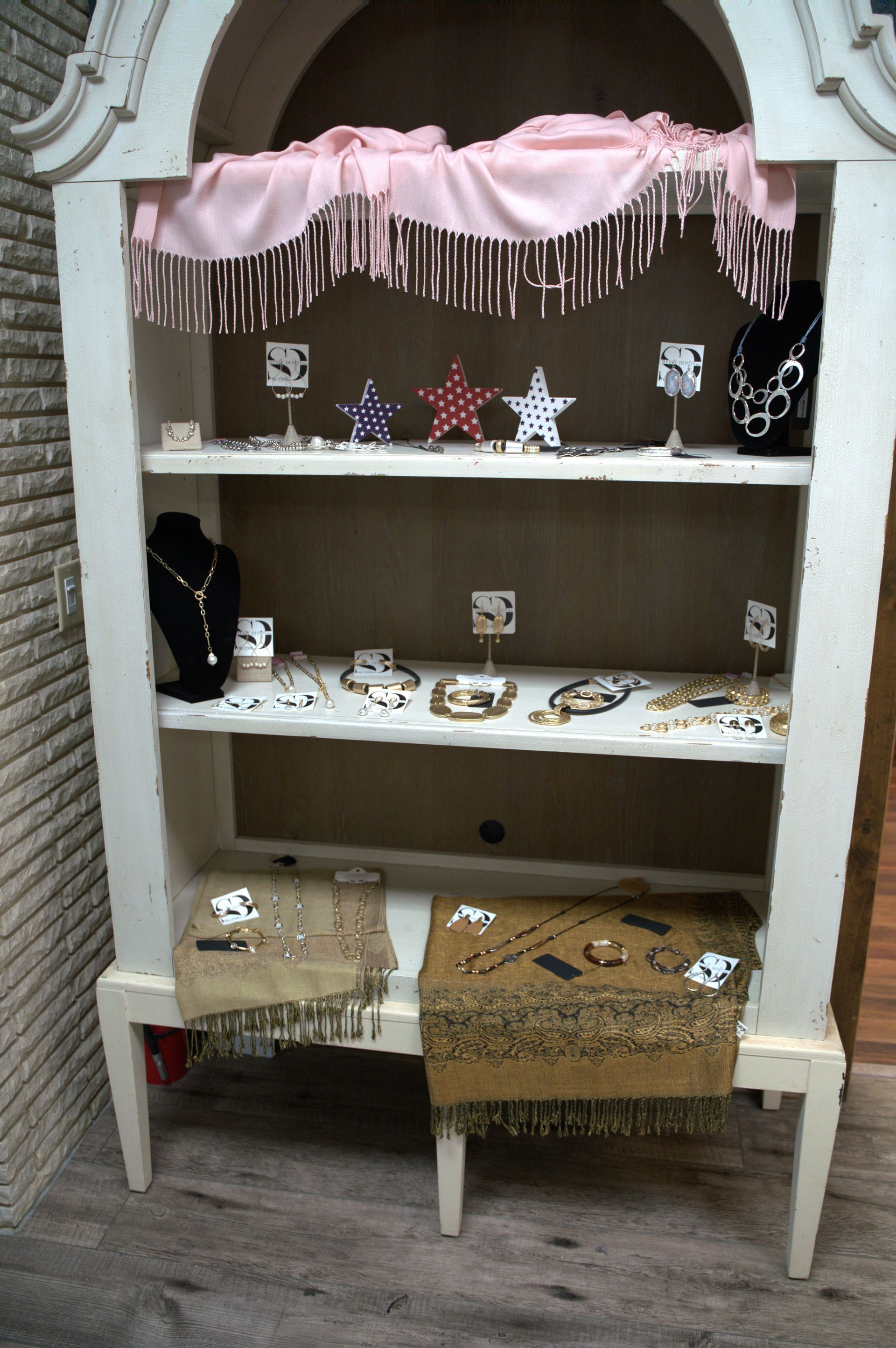 White jewelry display cabinet with several shelves holding various items.