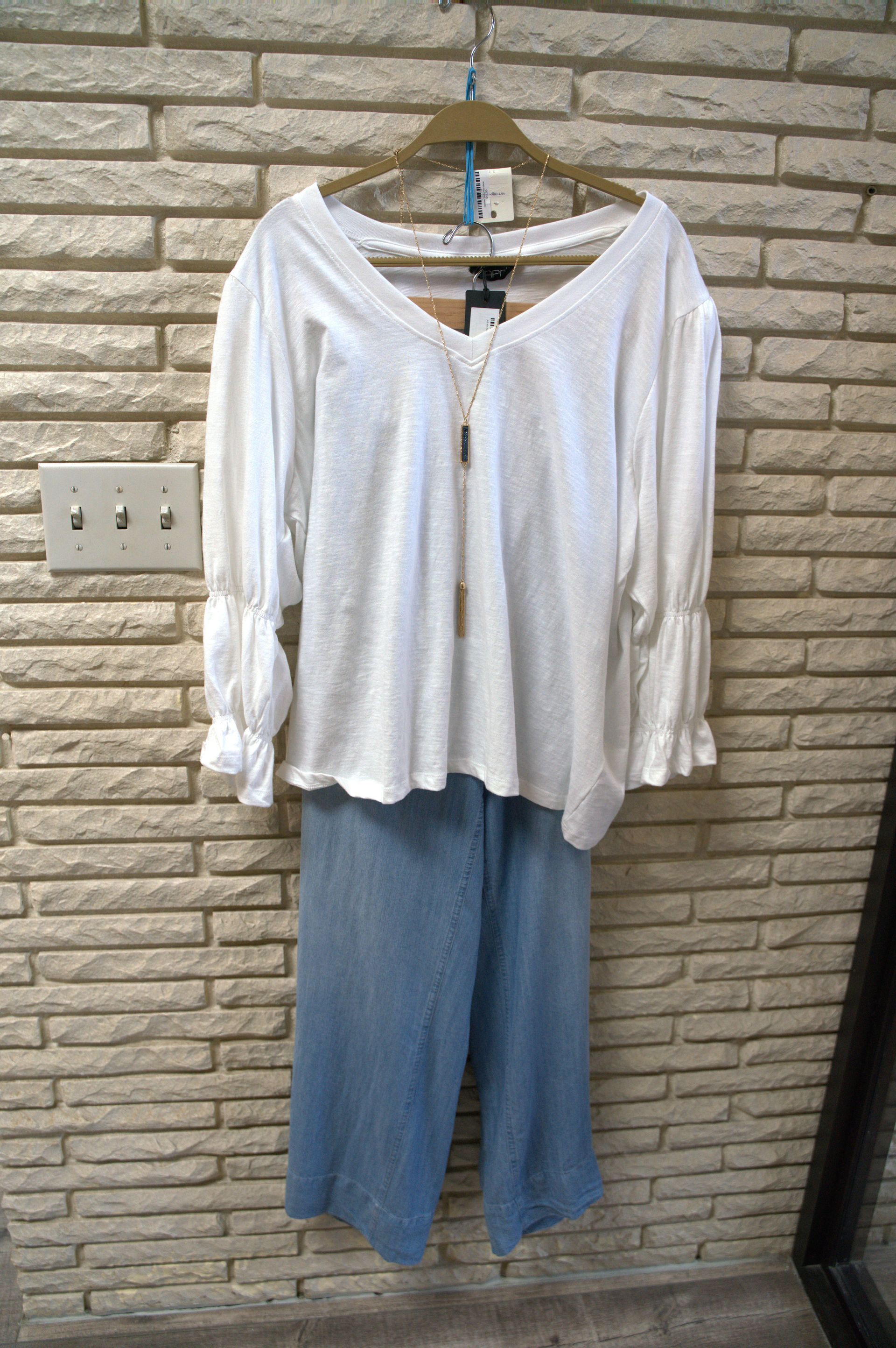 A white blouse with puffy sleeves and blue denim culottes hanging on a rack against a brick wall.
