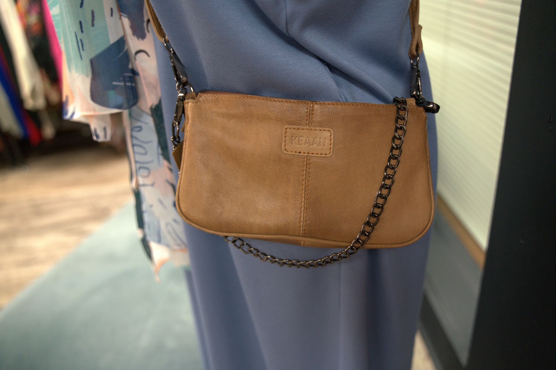 Tan leather crossbody bag with a chain strap against a light blue dress.