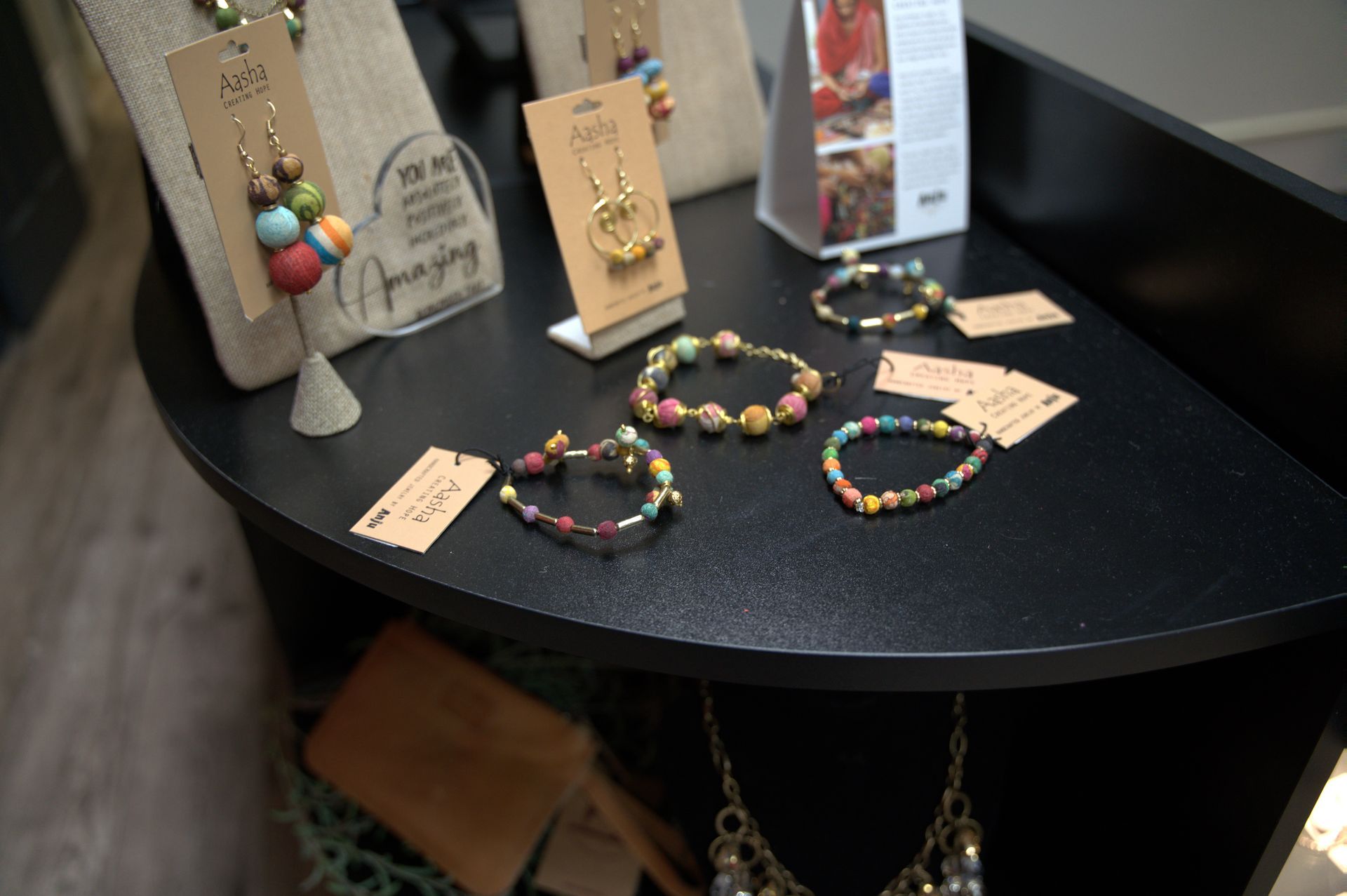Jewelry display on a black counter, featuring beaded bracelets and necklaces in various colors.  Some items have price tags.