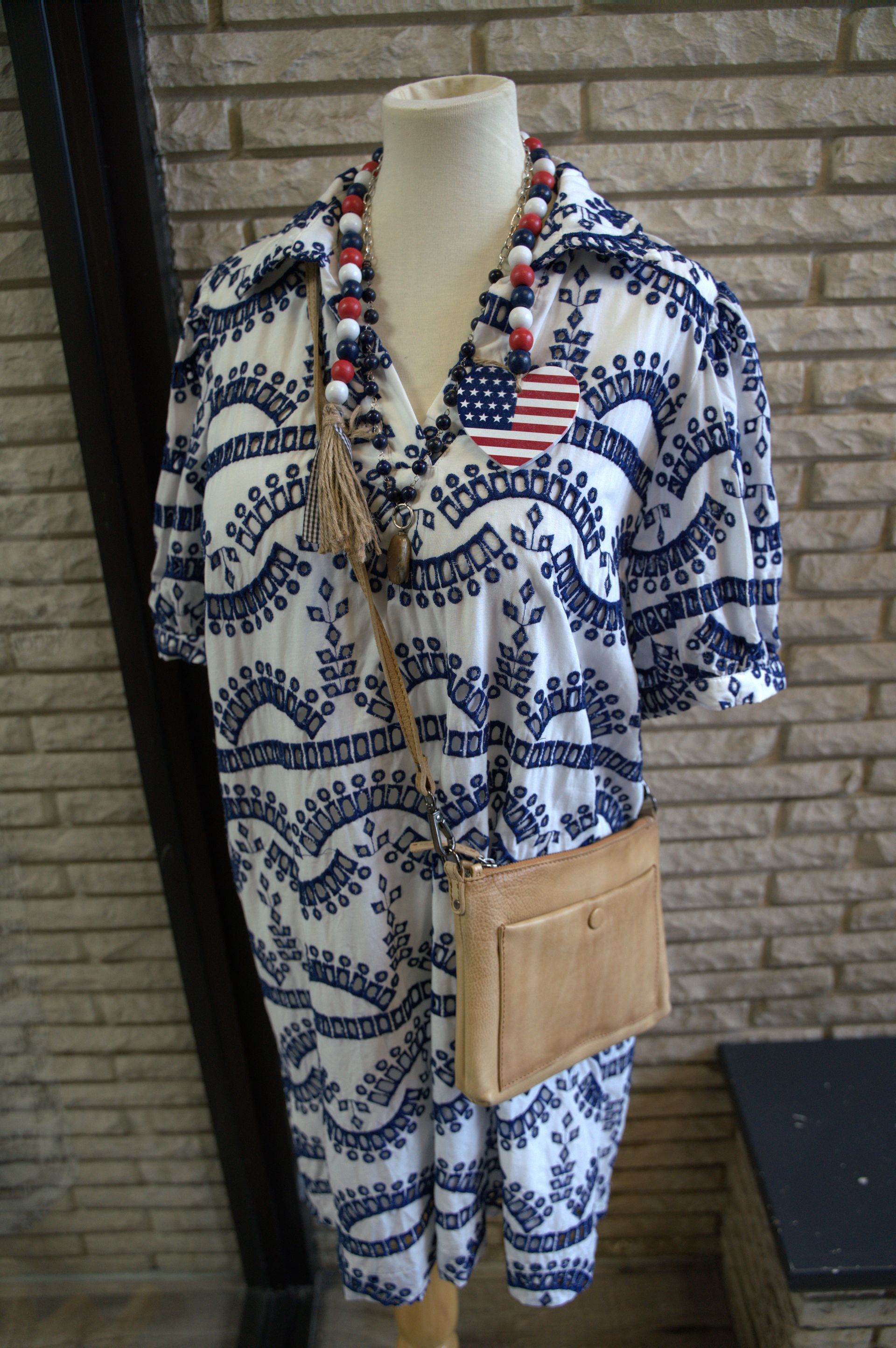 A white and blue patterned jumpsuit on a mannequin, accessorized with a beaded necklace and American flag patch.