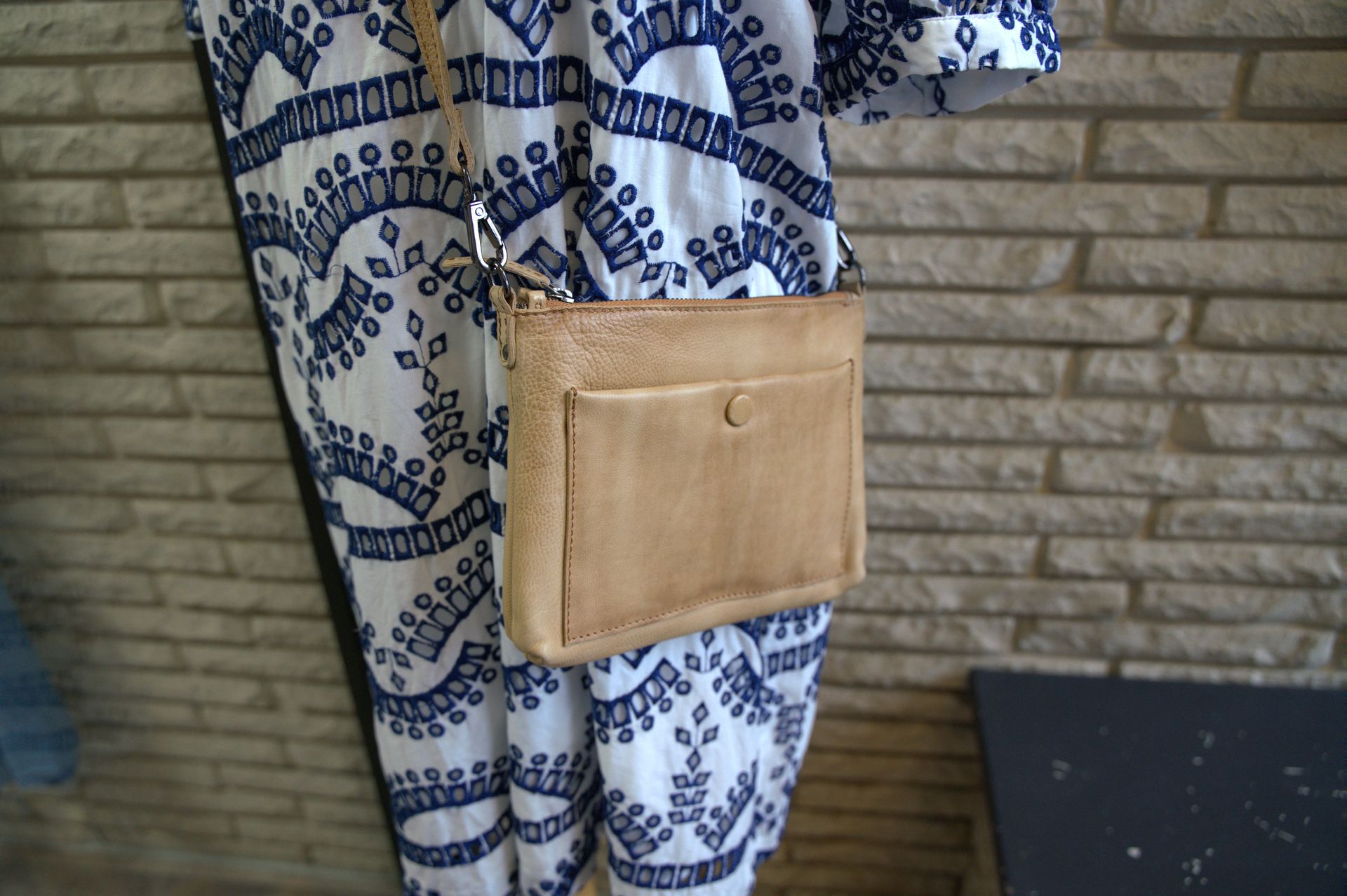 Tan crossbody bag worn over a white and blue patterned garment. Bag has a front pocket with a button.