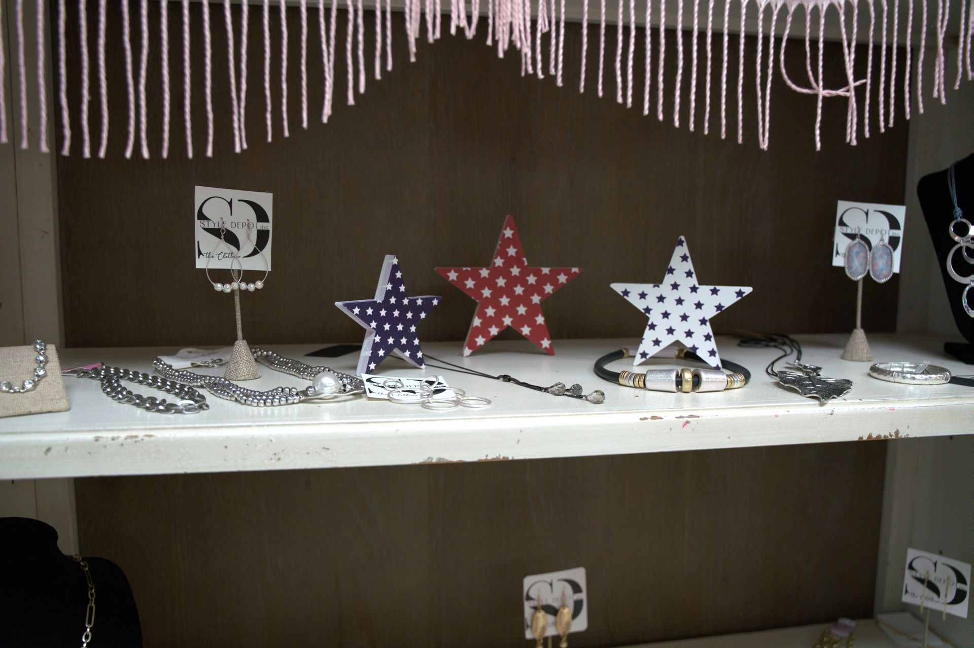 Jewelry display featuring necklaces, earrings, and star-shaped decorations in red, white, and blue on a white shelf.