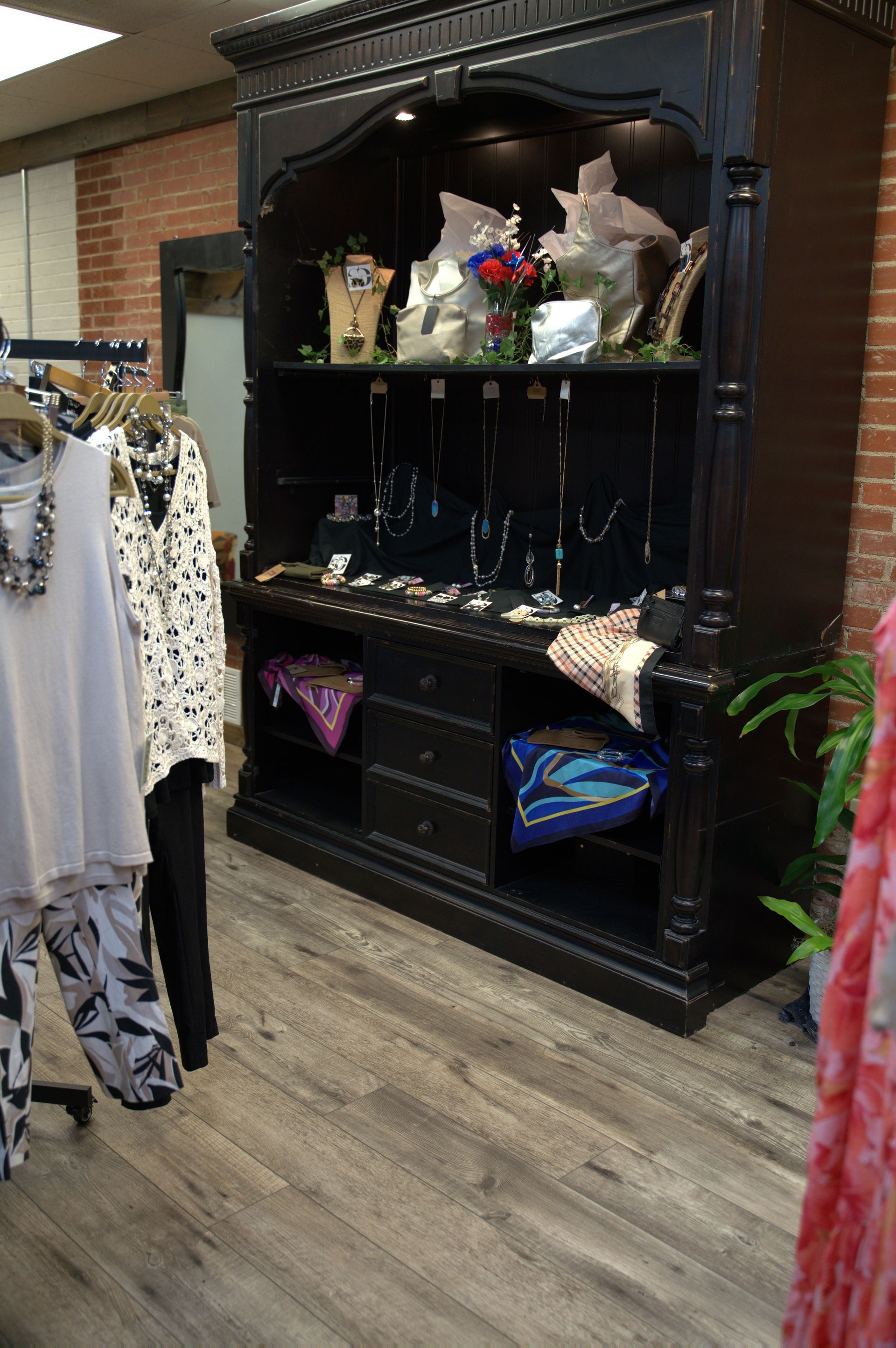 Black display cabinet in a store, showcasing jewelry and scarves. Clothing racks are on the left.