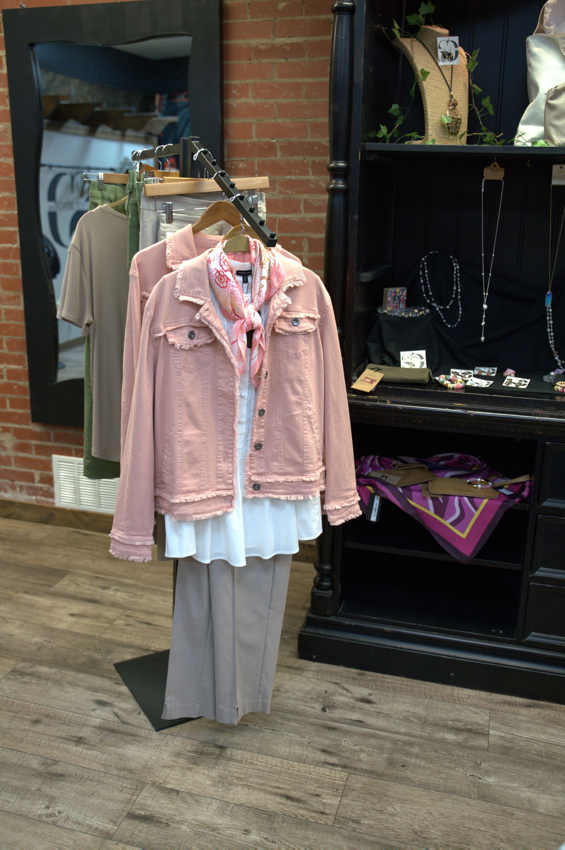 A retail display showcases a pink denim jacket, white shirt, and beige pants on a rack.