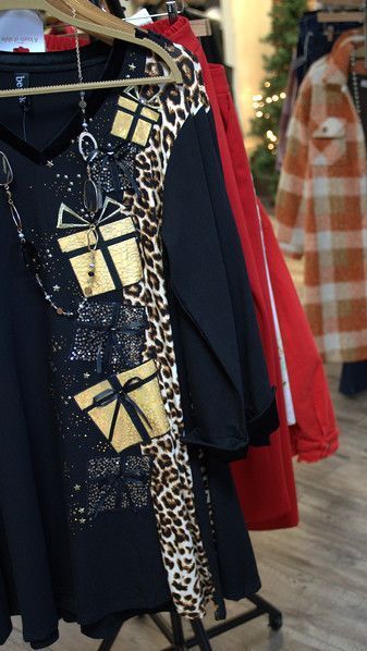 Black top with gold gift boxes and leopard print sleeve hanging on rack among other garments.