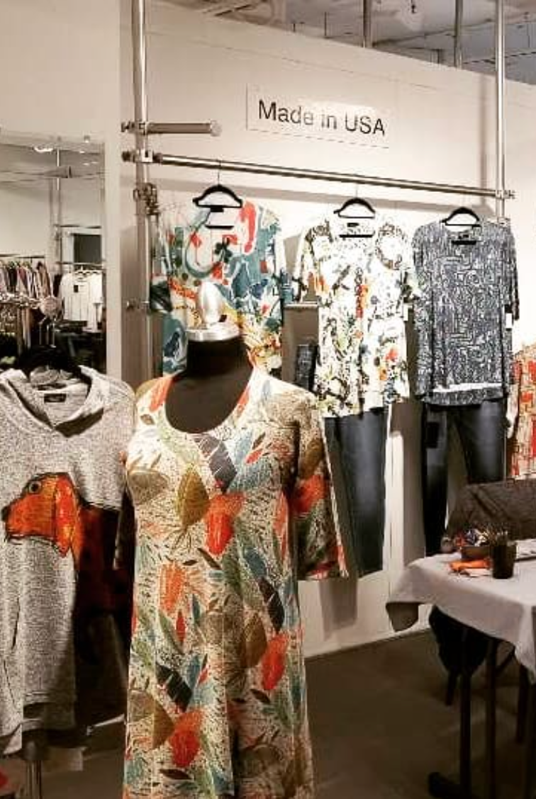 Clothing display in a store with mannequins wearing colorful tops and pants. Sign above reads