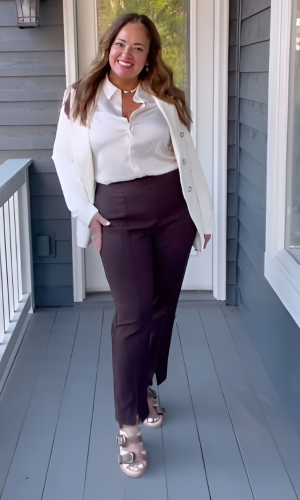 Woman in white shirt, blazer, and brown pants with gold sandals standing on a porch.