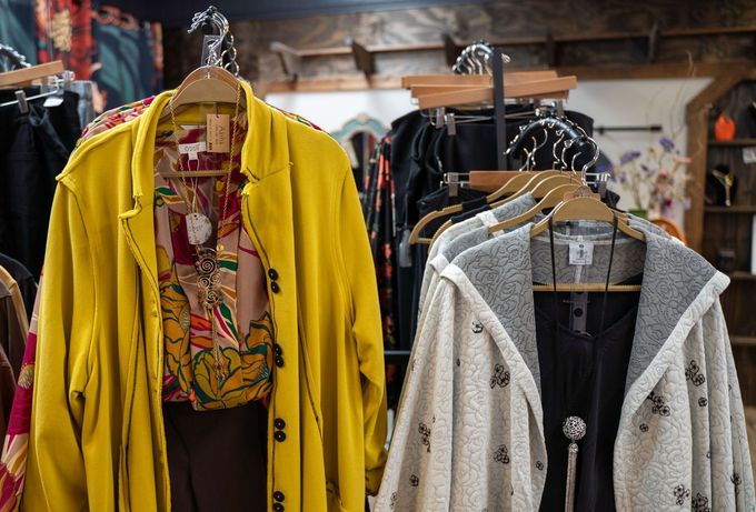 Clothing rack in a boutique featuring a bright yellow coat over a patterned shirt, and a hooded, off-white cardigan.