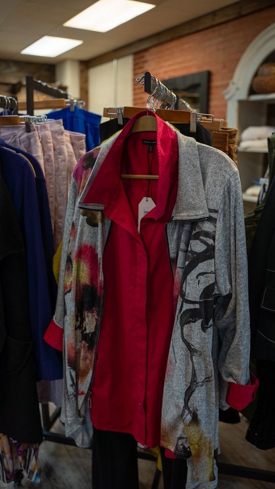 Clothing rack with a red shirt and a grey printed jacket with a red collar and cuffs. Inside a store.