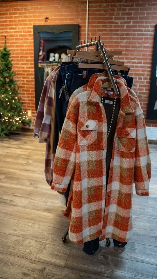 Clothing rack with various plaid jackets and coats in a boutique setting. A Christmas tree is visible in the background.