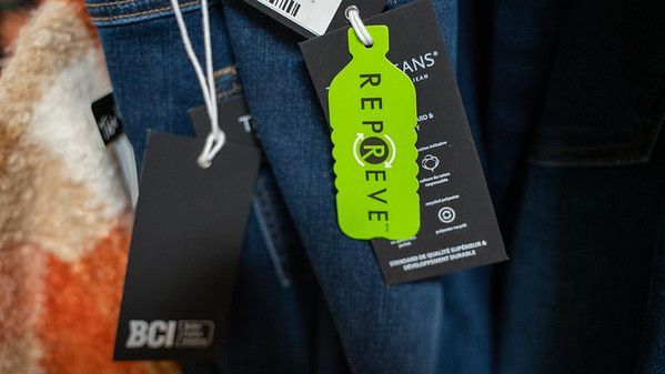 Close-up of jeans with several hang tags, including a bright green REPREVE tag with a recycling symbol.