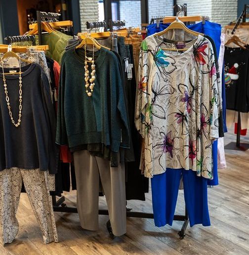 Clothing rack in a boutique displaying various tops, pants, and dresses.