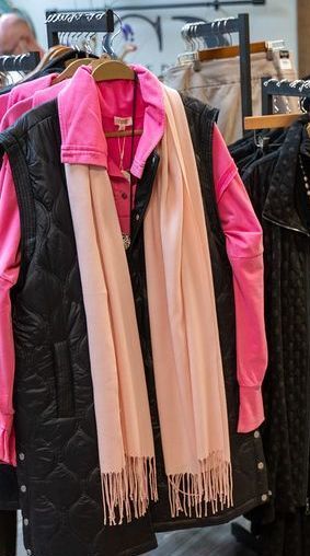 Clothes rack displaying a pink shirt, black quilted vest, and a pink scarf in a store.