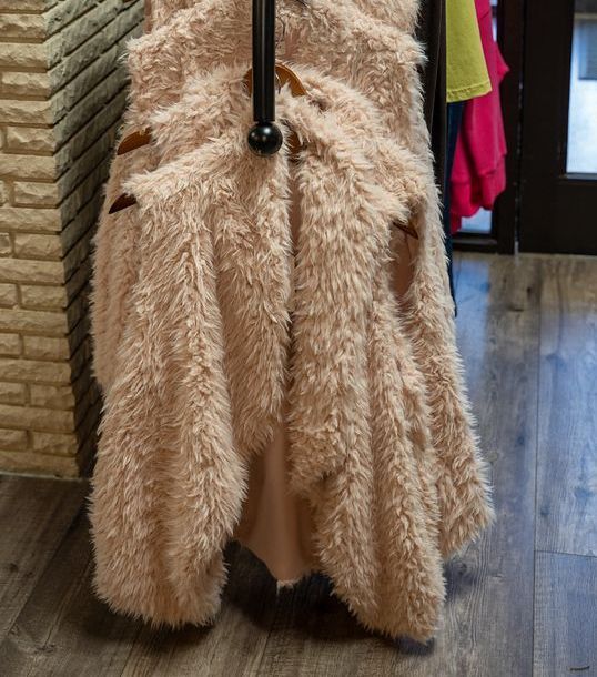 Pink fluffy vests hanging on a black rack, against a brick wall and wooden floor.