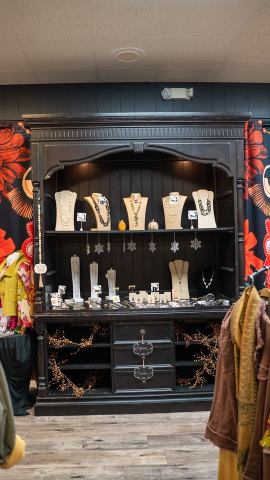 A black jewelry display case with necklaces and earrings on stands in a boutique. Wooden shelves and drawers.