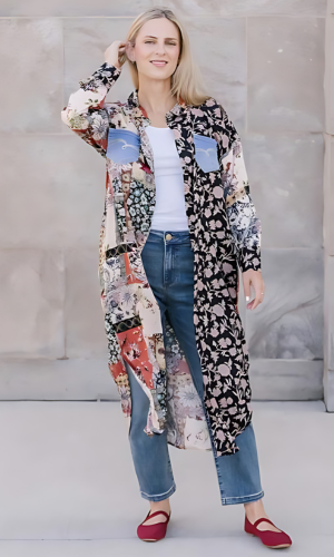 Woman in a long patterned shirt over a white tank top and jeans, wearing red shoes. Posing outdoors.