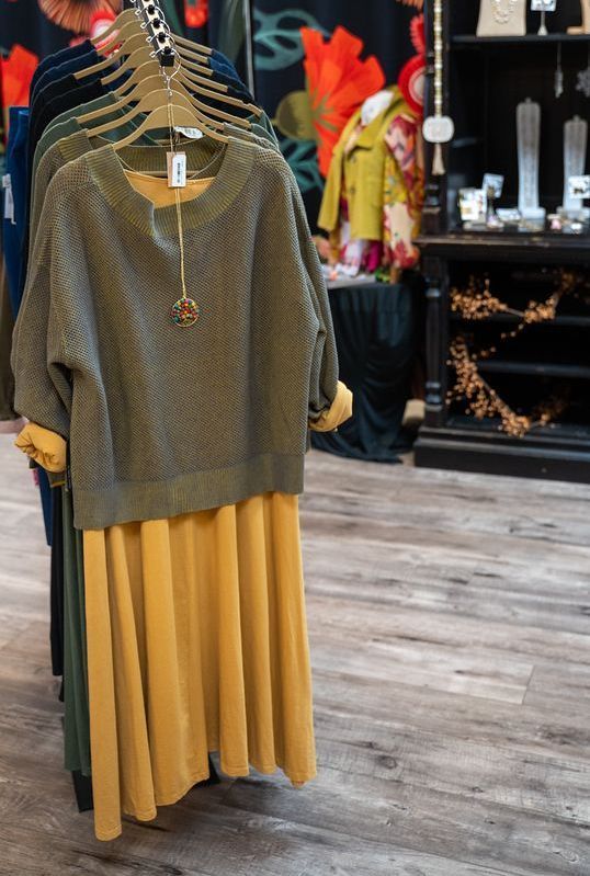 Clothing rack displaying an olive green sweater over a mustard yellow dress in a boutique.