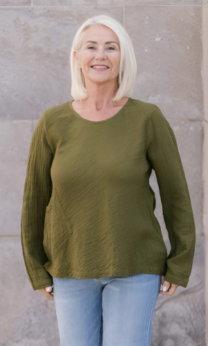 Woman with blonde hair smiles, wearing an olive-green textured top.