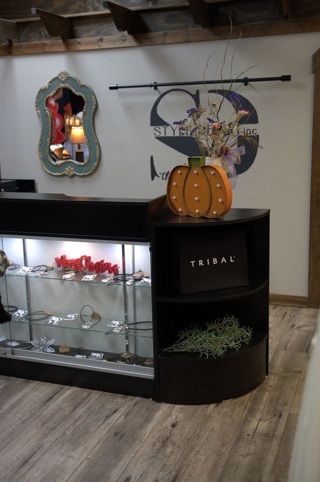 A store counter with a pumpkin decoration and a mirrored wall hanging. Display case with jewelry on the left.