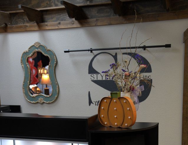 Interior with a decorative pumpkin, mirror, and floral arrangement on a counter. A logo is visible on the wall.