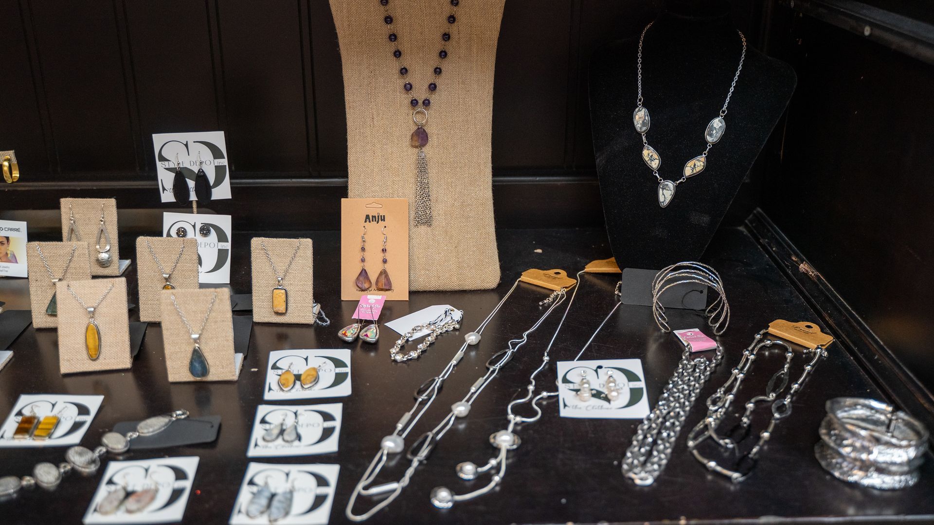 Jewelry display with necklaces, earrings, and bracelets on a dark surface. Some pieces are displayed on small stands.