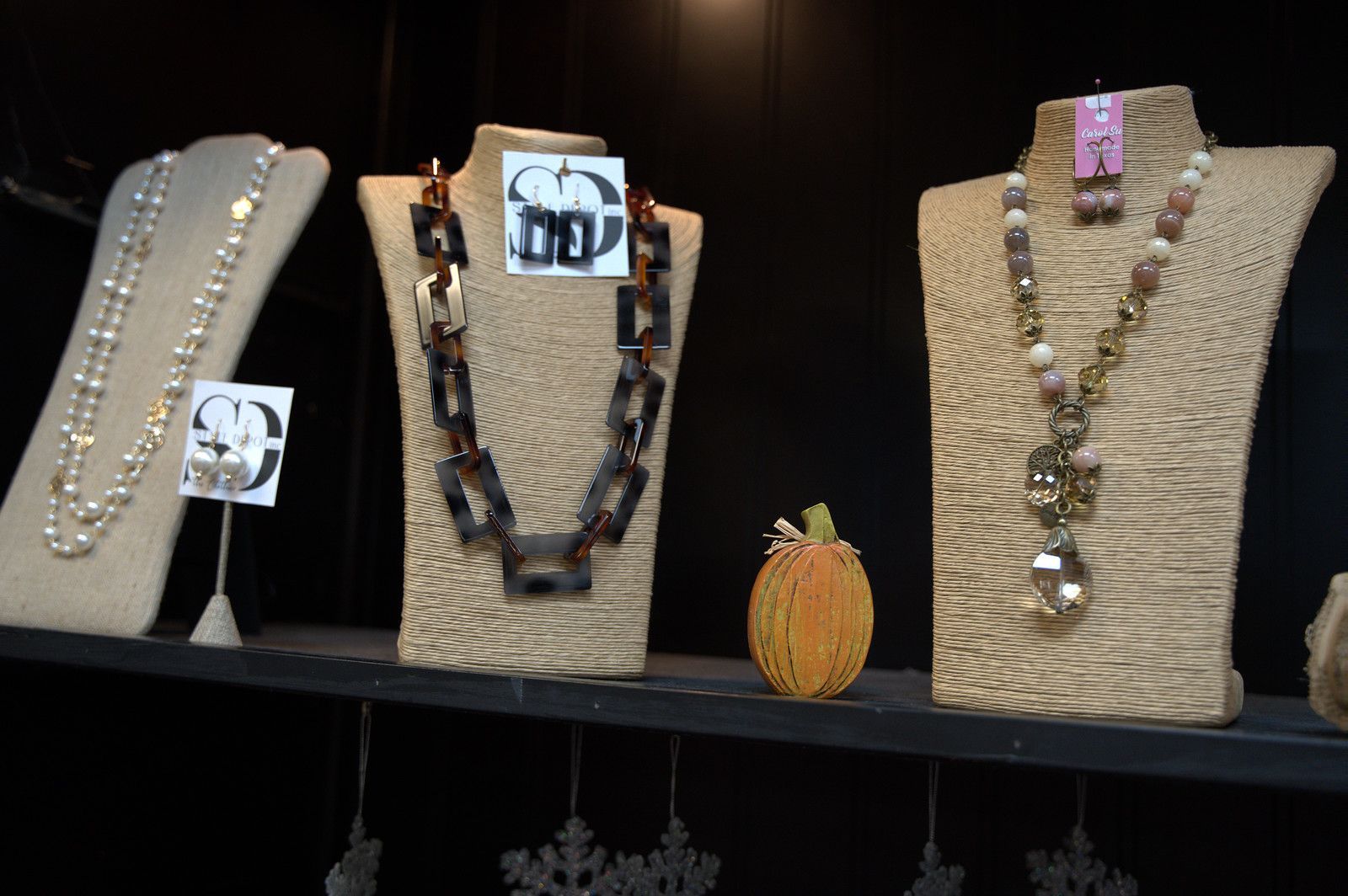 Jewelry display: necklaces on bust forms, including pearls, chain, and beaded designs, in a shop setting.