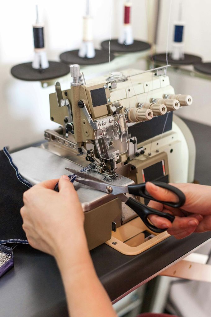 A person using scissors to trim fabric on an overlock sewing machine with various colored thread spools in the background.