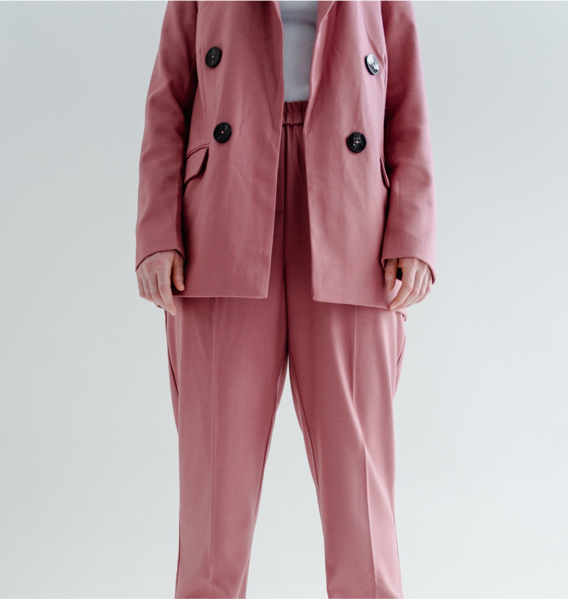 Blonde woman with albinism in a rose-colored suit, hand to her head, in a white studio setting.