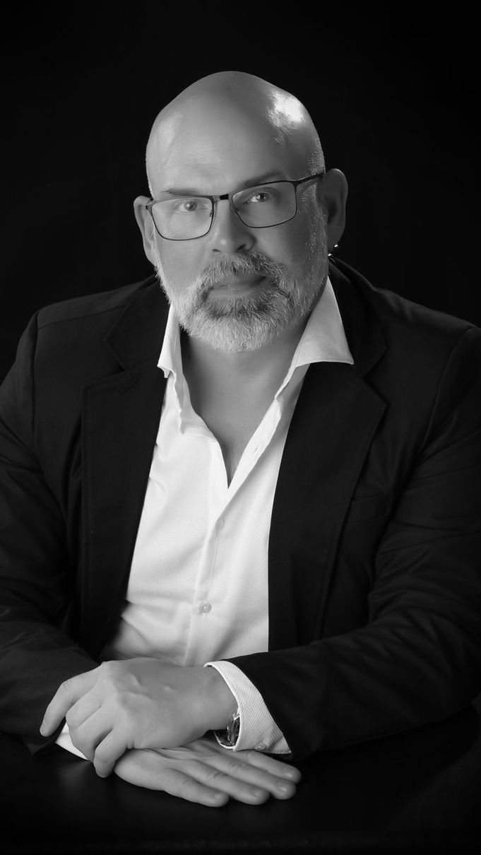Black and white portrait of a middle-aged man with glasses, a goatee, and a suit jacket, sitting and looking forward.